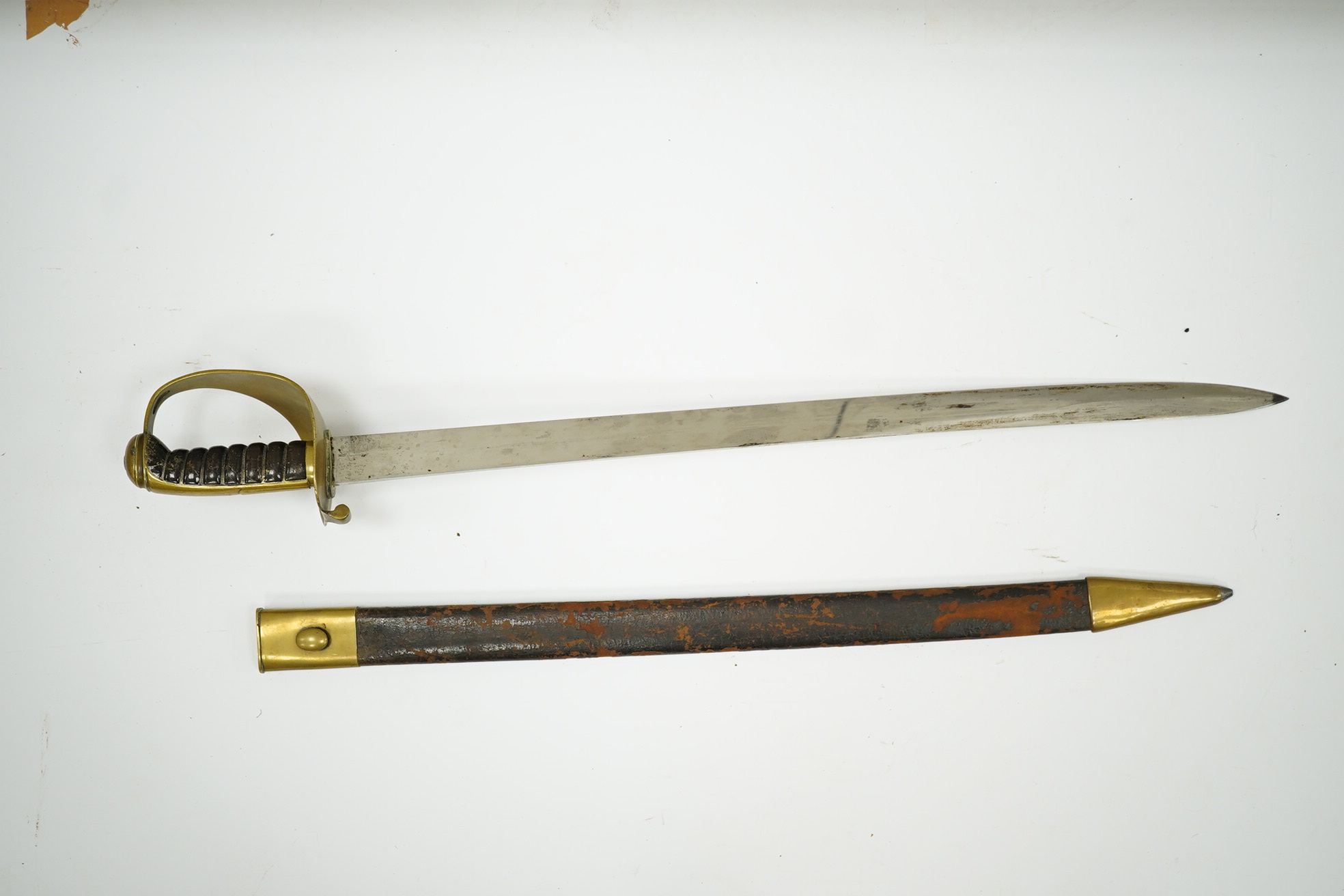 A late 19th century boarding cutlass with plain blade, plain brass guards and mounts, and leather covered grip, in its brass mounted leather scabbard (the chape is an associated replacement). Condition - fair